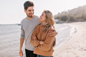 Jeune couple heureux posant ensemble en plein air près de la mer, illustrant l’amour et la complicité dans une relation.