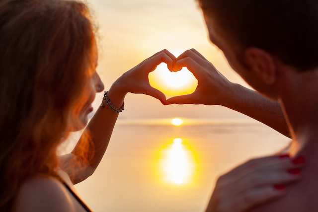 Un couple qui fait un cœur avec leurs mains devant un couché de soleil