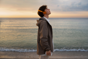 Homme avec un casque écoutant au bord de la mer, symbolisant la relaxation et la méditation